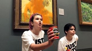 A protestor holds a can of tomato soup in front of a painting. 